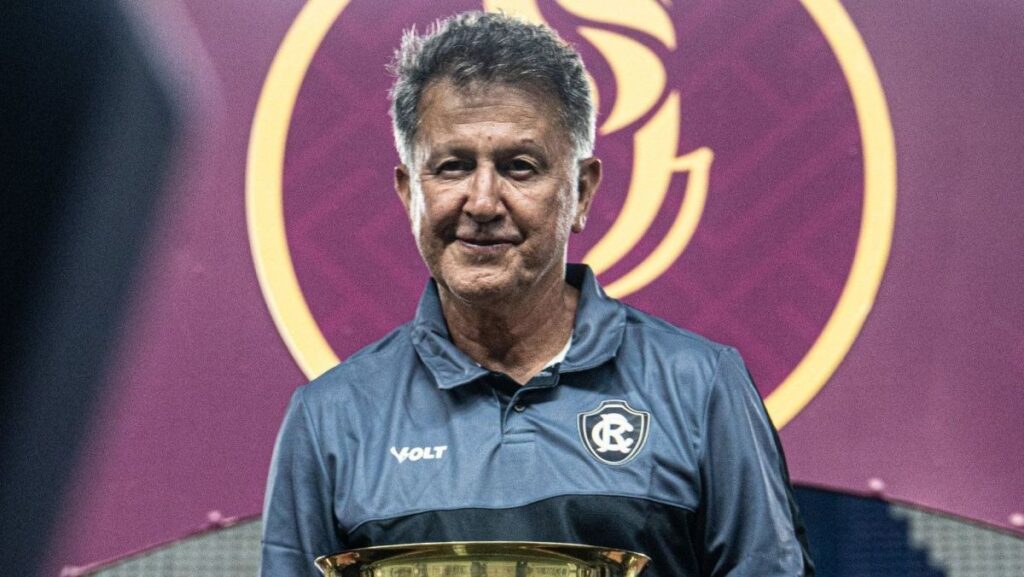Homem sorridente com camisa de time (Remo) e troféu dourado.