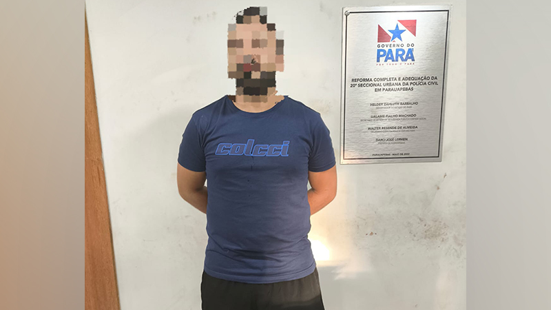 Homem com rosto censurado usando camiseta Colcci azul e shorts escuros, em frente a uma parede branca com uma placa do Governo do Pará.