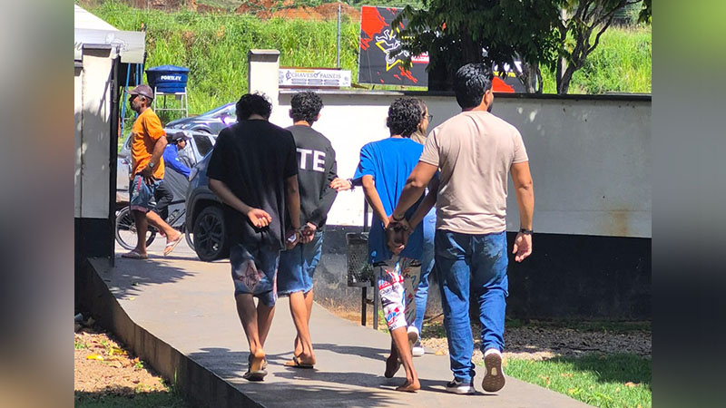 Grupo de homens algemados sendo escoltados em área externa.