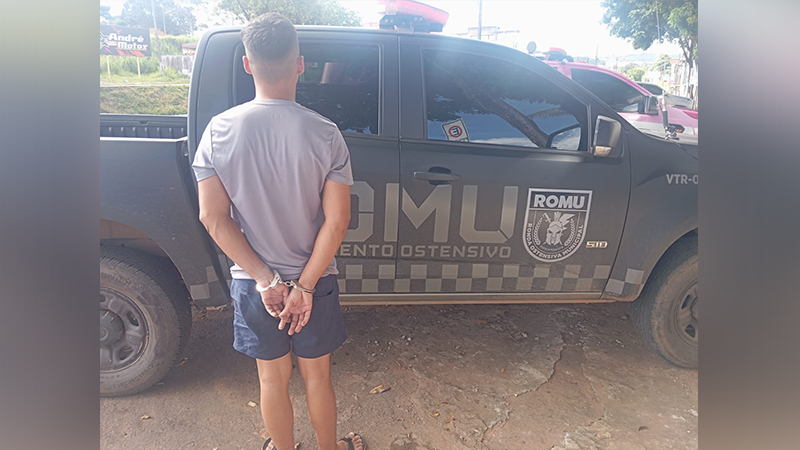 Homem algemado de costas para a câmera em frente a uma viatura da ROMU.