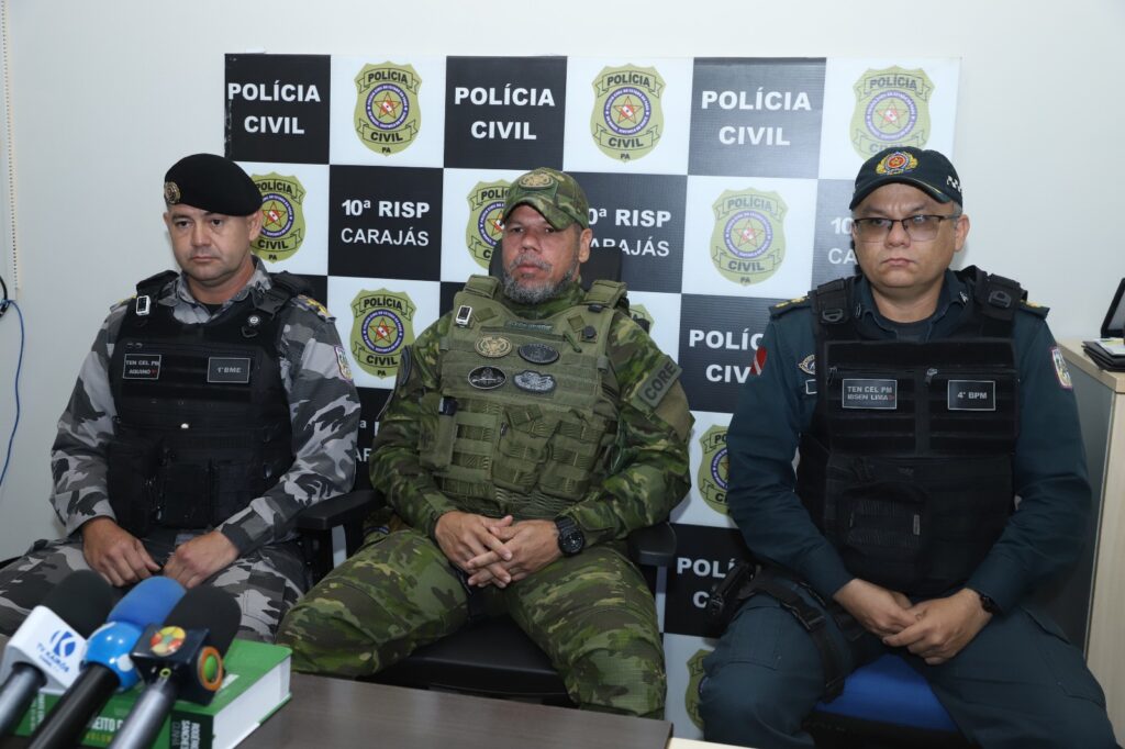 Três policiais sentados em uma coletiva de imprensa com o fundo da Polícia Civil e 10ª RISP Carajás.