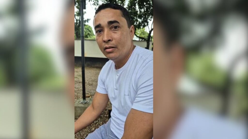 Homem em camiseta branca olhando para a câmera ao ar livre.