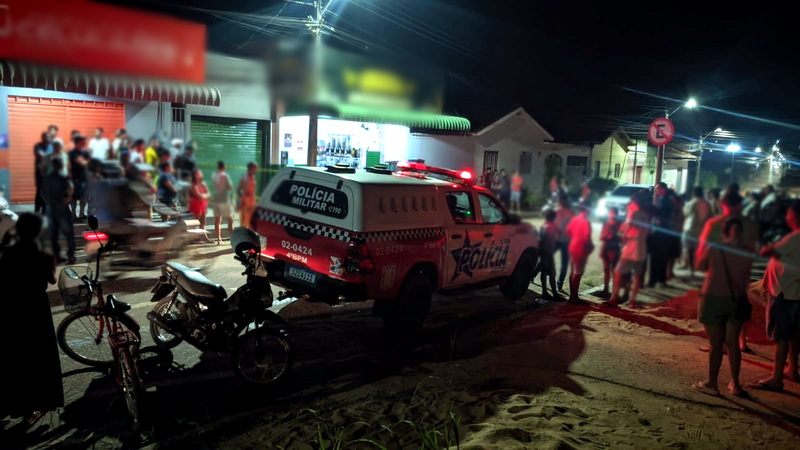Viatura da Polícia Militar e multidão reunida em rua à noite.