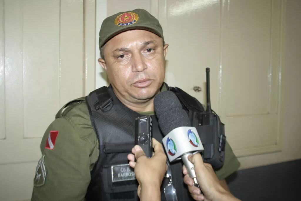 Homem fardado, possivelmente policial ou militar, sendo entrevistado por repórteres.