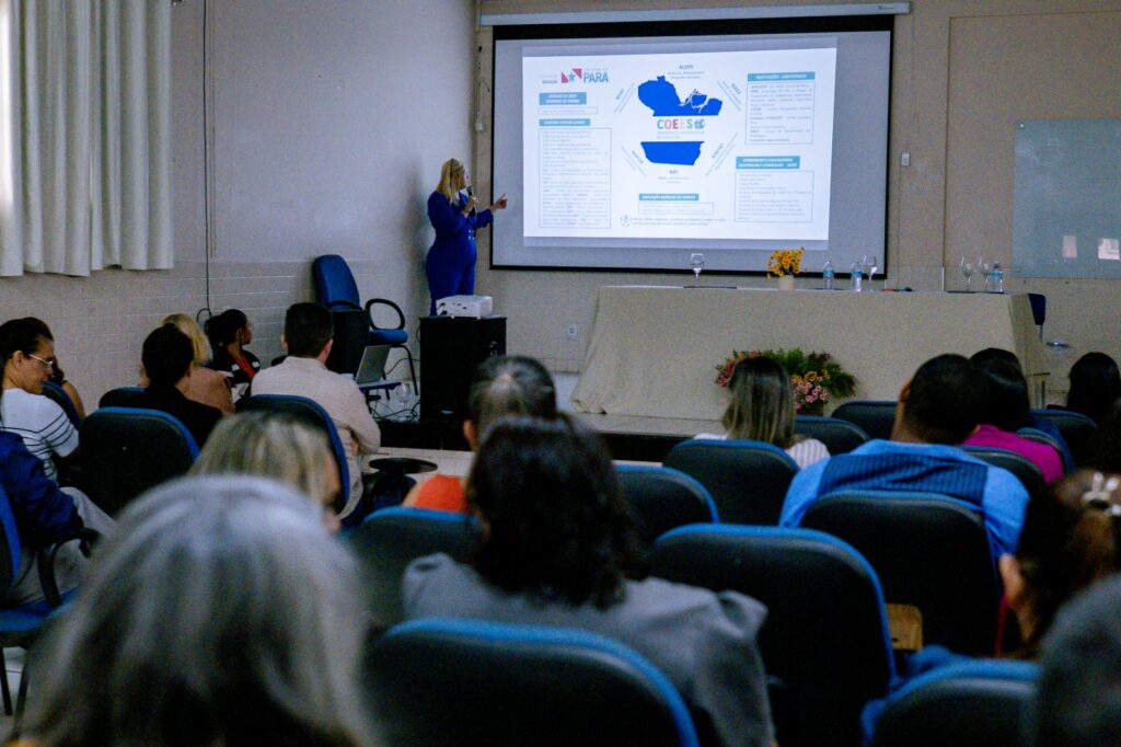 Mulher de azul apresentando slide sobre o Pará e COES para uma plateia em auditório.