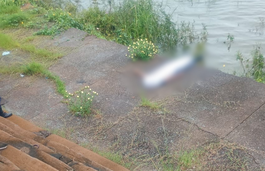 Corpo borrado de uma pessoa deitada em concreto à beira da água, com vegetação ao redor.