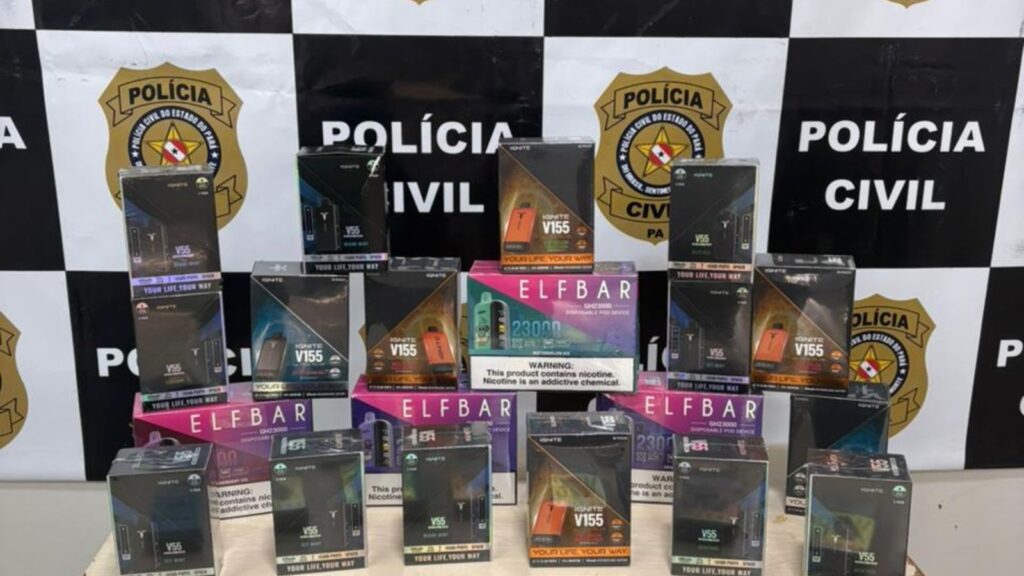 Caixas de vapes Ignite V155 e Elfbar apreendidas, com o logo da Polícia Civil ao fundo.