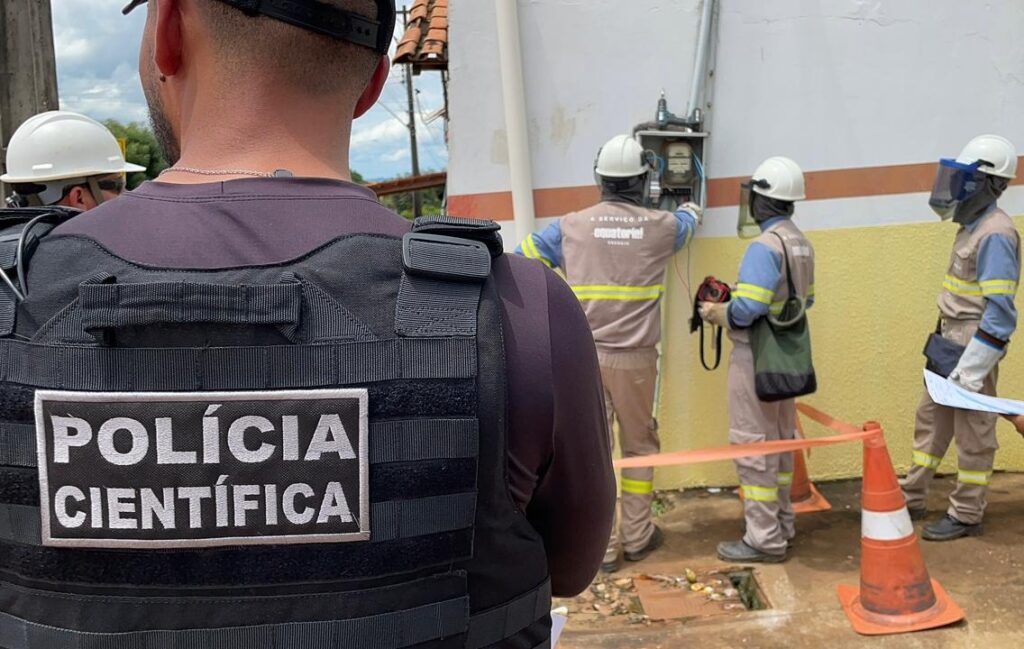 Policial da Polícia Científica observa técnicos da Equatorial em inspeção de medidor de energia.