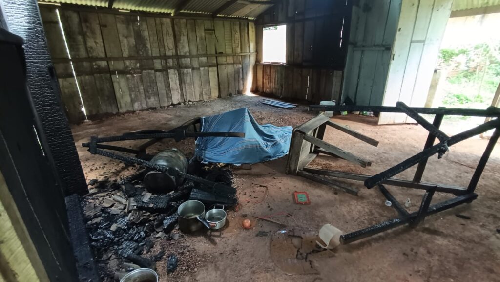 Interior de casa simples destruída por fogo, com móveis queimados e objetos espalhados.