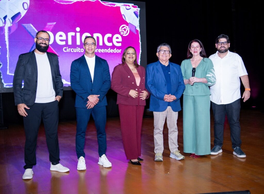 Grupo de seis pessoas (três homens e três mulheres) posando no palco em frente a uma tela com o logo 'Xperience Circuito Empreendedor'.