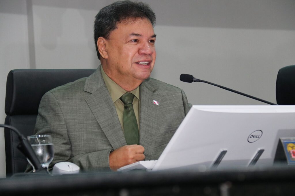 Homem em terno e gravata falando ao microfone em um evento.