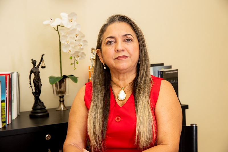 Retrato de mulher de meia-idade com cabelos grisalhos e blusa vermelha em escritório.