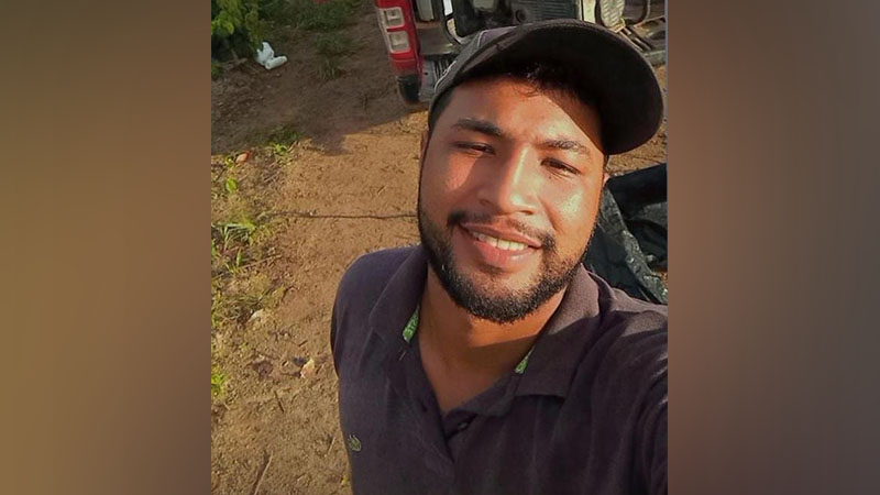 Homem jovem sorrindo com boné e barba em ambiente externo.