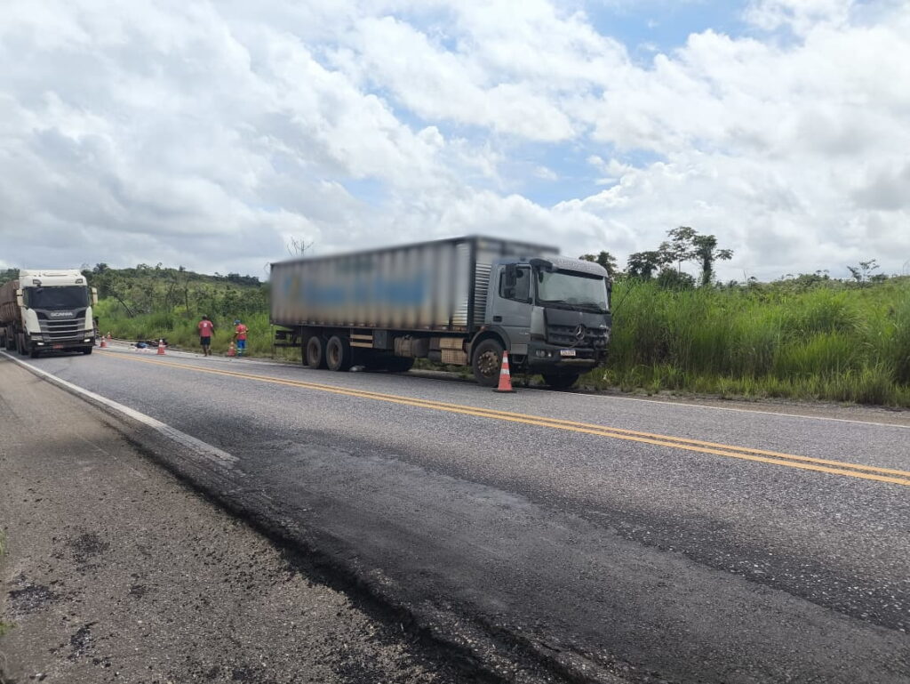 Caminhão cinza danificado parado na lateral de uma rodovia com cones.