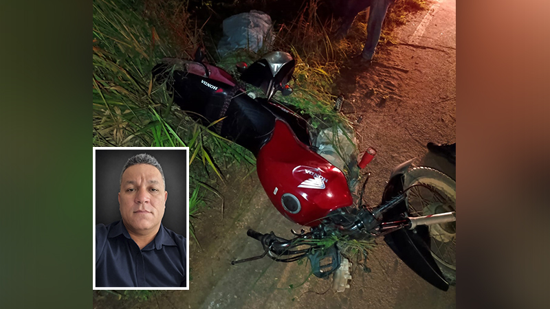 Motocicleta Honda vermelha e preta tombada na grama, com foto de homem em destaque.