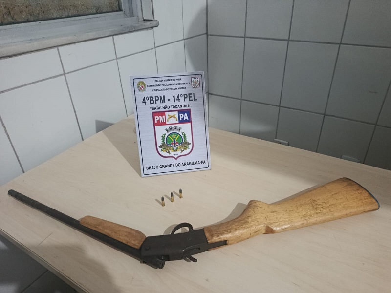 Arma de fogo caseira e três munições sobre uma mesa, com placa da Polícia Militar do Pará ao fundo.