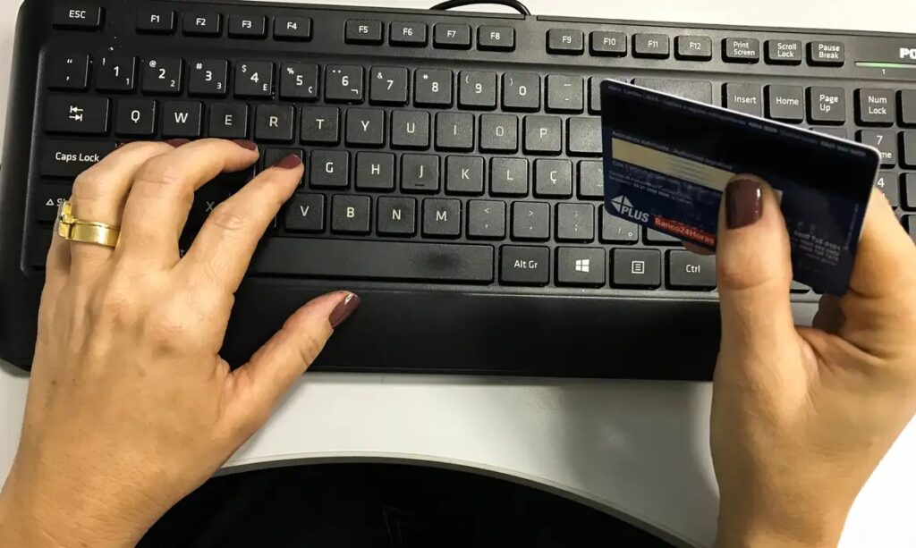 Mãos sobre teclado preto segurando um cartão de crédito para compras online.