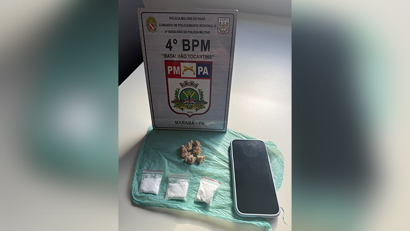 Placa da Polícia Militar do Pará, porções de drogas (crack e pó branco) e um celular em cima de um plástico verde.
