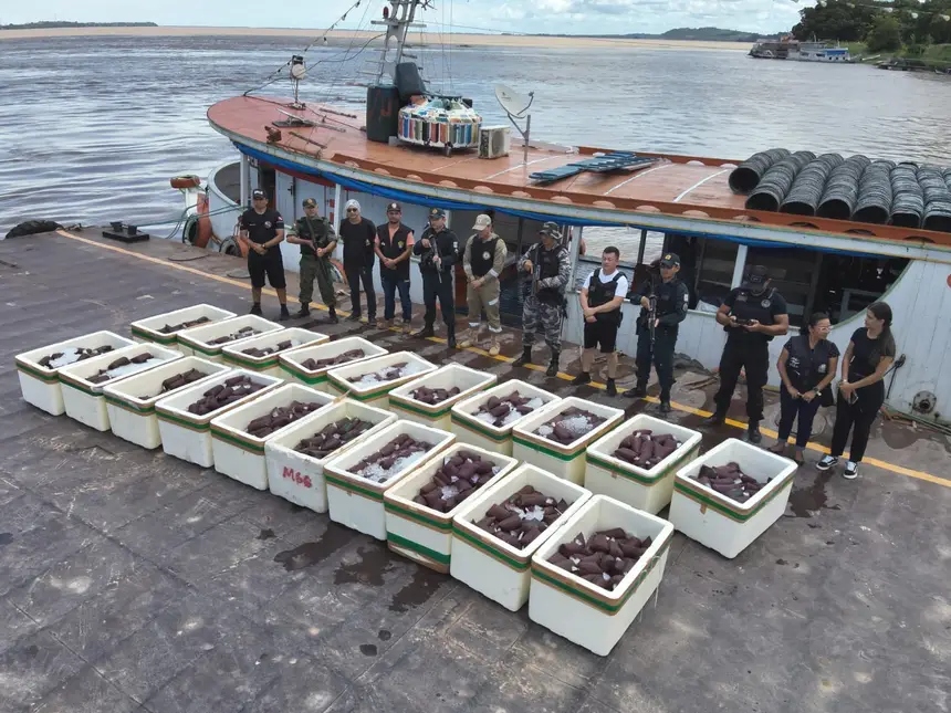 Grupo de agentes de segurança ao lado de caixas de isopor cheias de peixe e um barco grande.