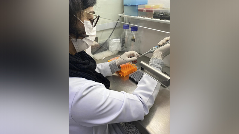 Cientista com máscara e luvas operando uma pipeta em laboratório.