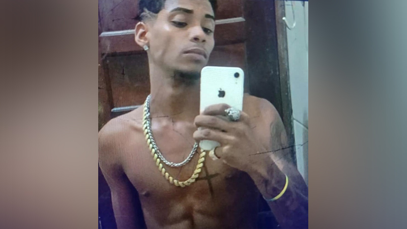 Jovem sem camisa com correntes tirando uma selfie com iPhone branco.