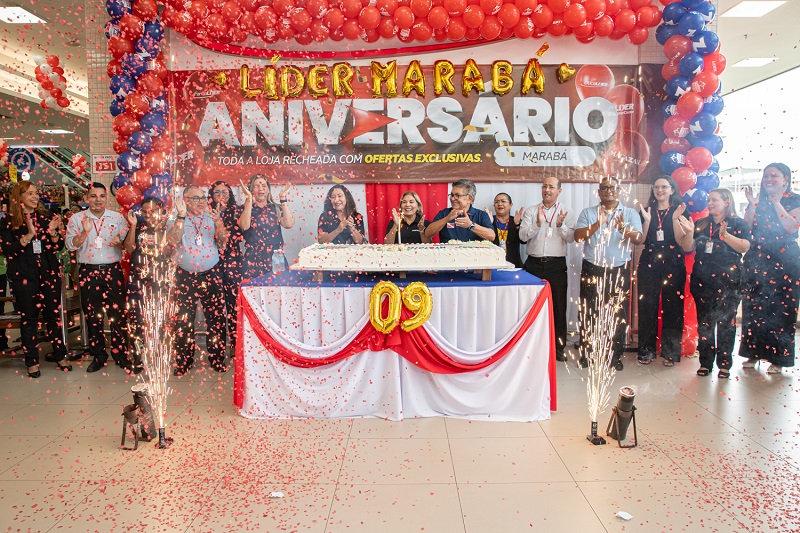 Grupo de funcionários celebrando o 9º aniversário do Líder Marabá com bolo gigante, confete e fogos indoor.