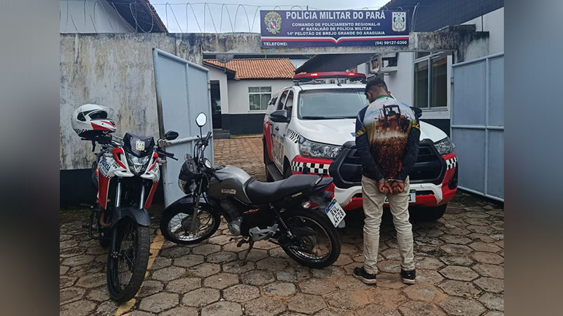 Homem algemado de costas, duas motos e viatura da Polícia Militar do Pará em frente a um batalhão.