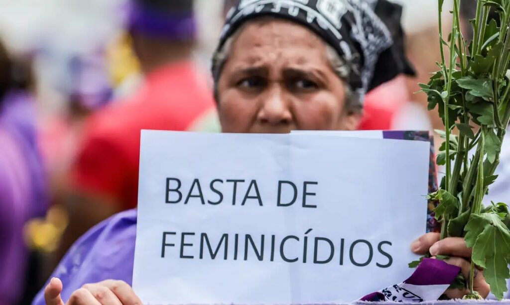 Mulher segurando cartaz 'BASTA DE FEMINICÍDIOS' em protesto.