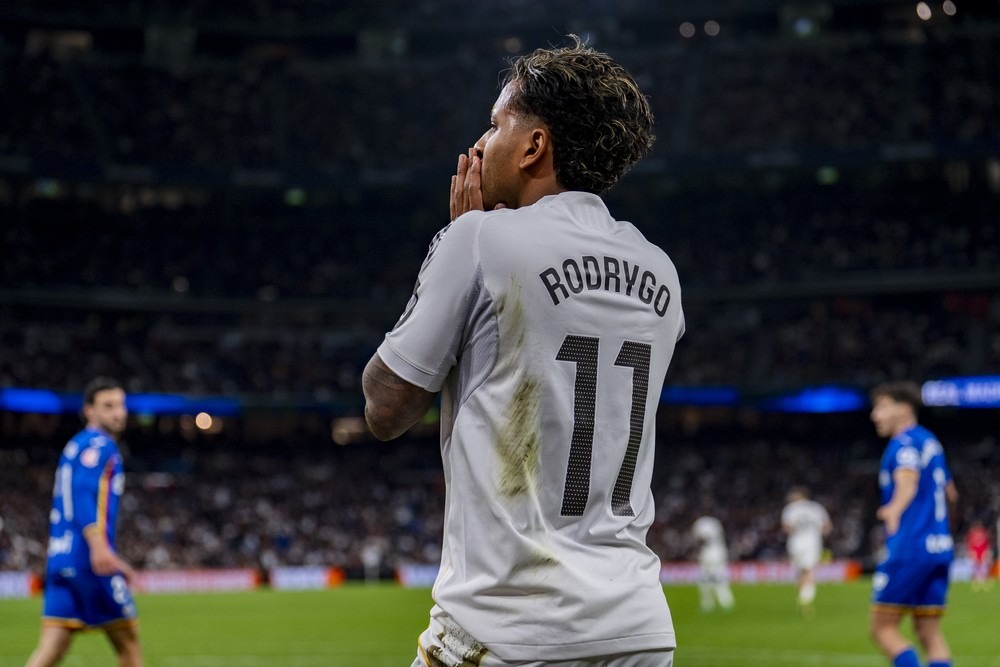 Rodrygo, jogador do Real Madrid, com a camisa 11, em campo de futebol, com as mãos no rosto.