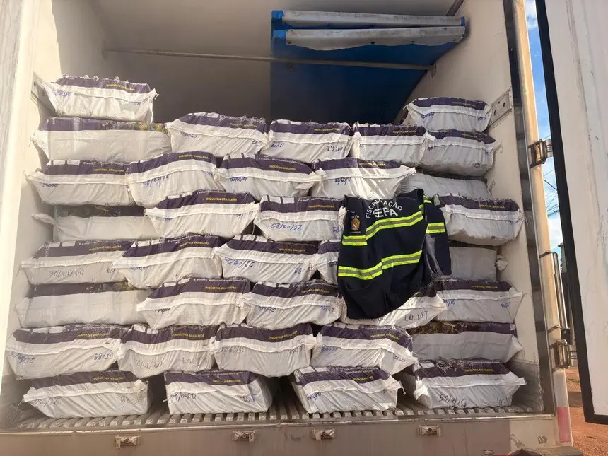 Interior de caminhão ou contêiner com inúmeras embalagens empilhadas e um colete de fiscalização.