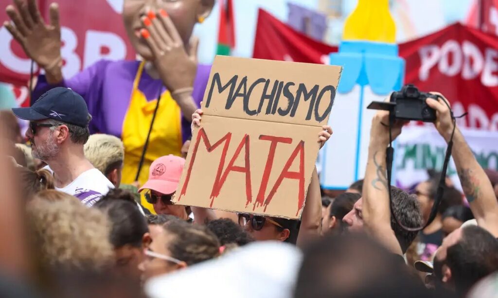 Pessoa em manifestação segurando um cartaz de papelão com a frase 'MACHISMO MATA'.