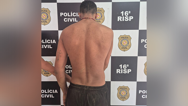 Homem de costas, sem camisa, em frente a um painel da Polícia Civil.