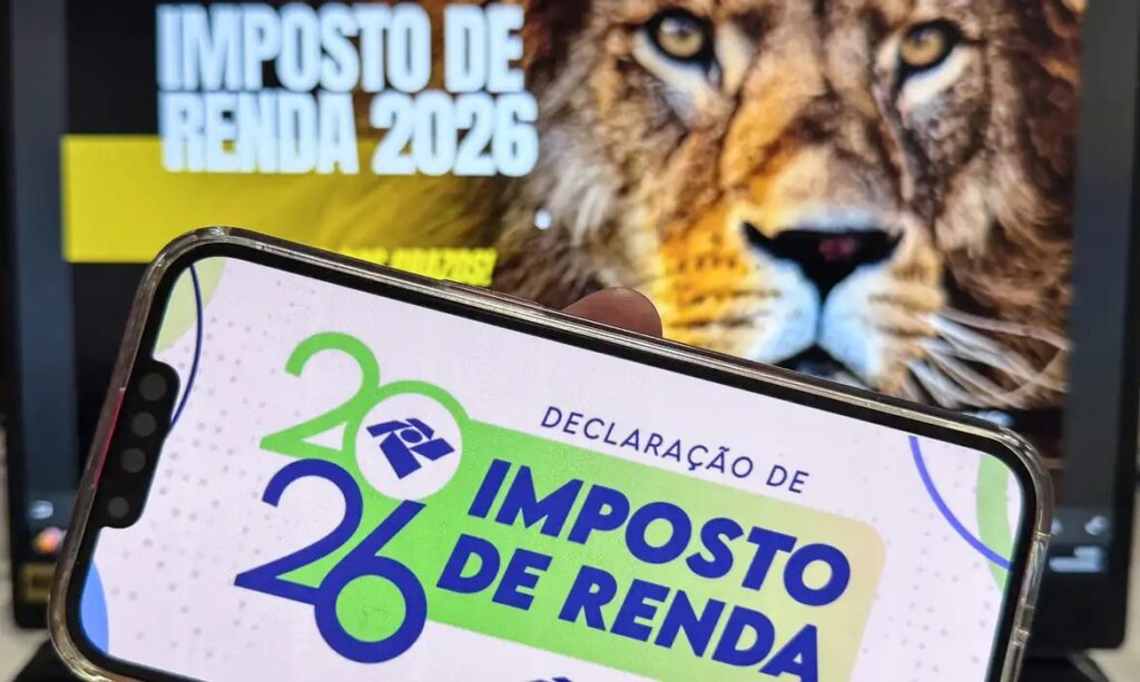Foco no smartphone com a Declaração de Imposto de Renda 2026 e o logo da Receita Federal, com um leão desfocado ao fundo.