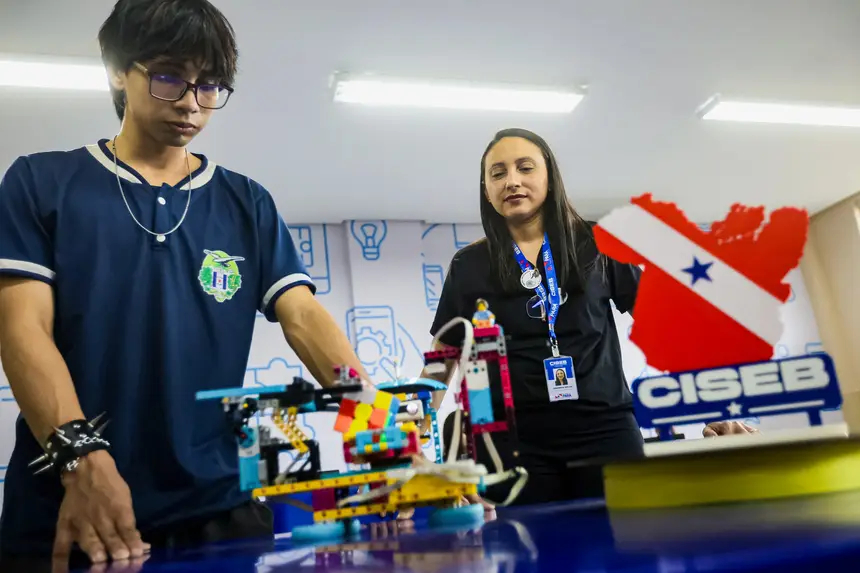 Jovem e mulher observando um robô colorido de blocos em um evento de robótica educacional.
