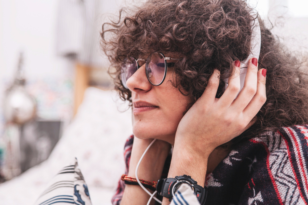 Pessoa de cabelo cacheado com óculos e fones de ouvido brancos.