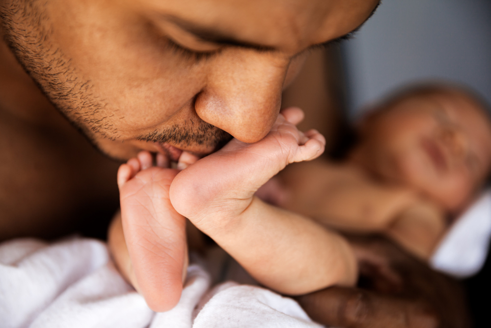 Homem beijando os pés de um bebê recém-nascido em um cobertor branco.