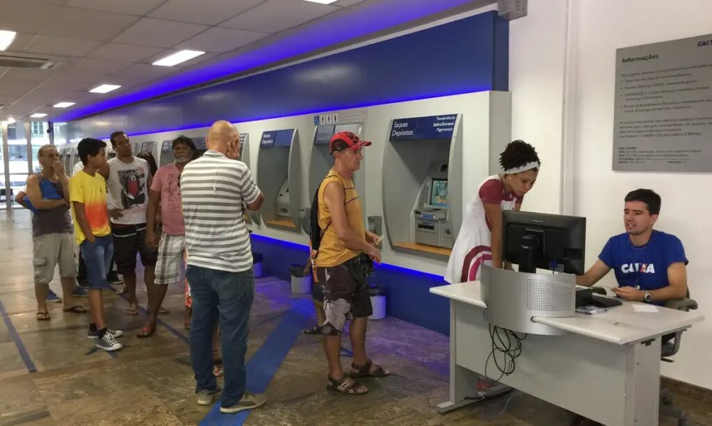 Pessoas em fila utilizando caixas eletrônicos em uma agência bancária.