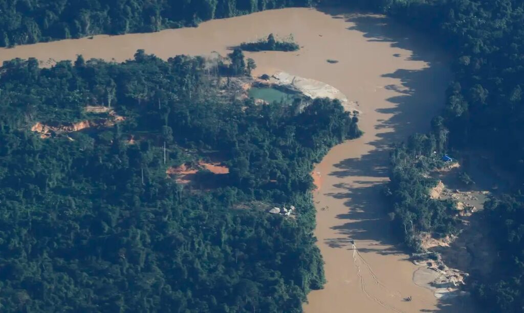 Vista aérea de desmatamento e garimpo ilegal próximo a um rio barrento na floresta amazônica.