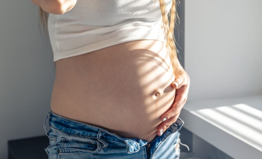 Barriga de grávida com calça jeans e sombra de persiana.