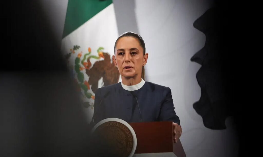 Mulher em púlpito com a bandeira do México ao fundo.