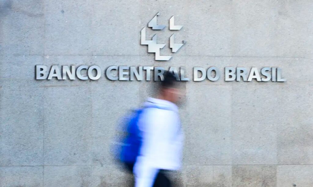 Letreiro e logotipo do Banco Central do Brasil na parede com pessoa em movimento.