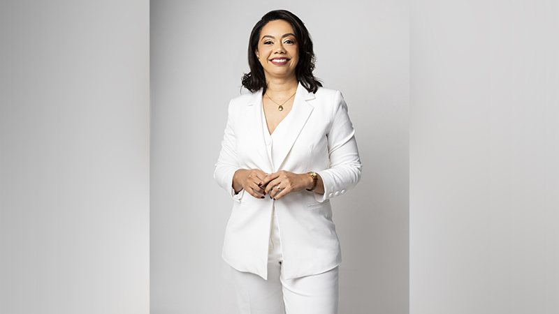 Mulher sorridente de blazer e calça brancos em estúdio.