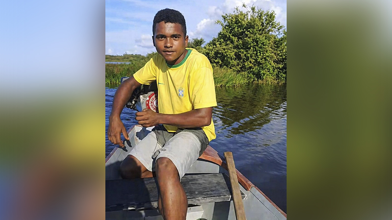 Jovem em camiseta do Brasil em barco a motor, em ambiente natural aquático com vegetação densa.