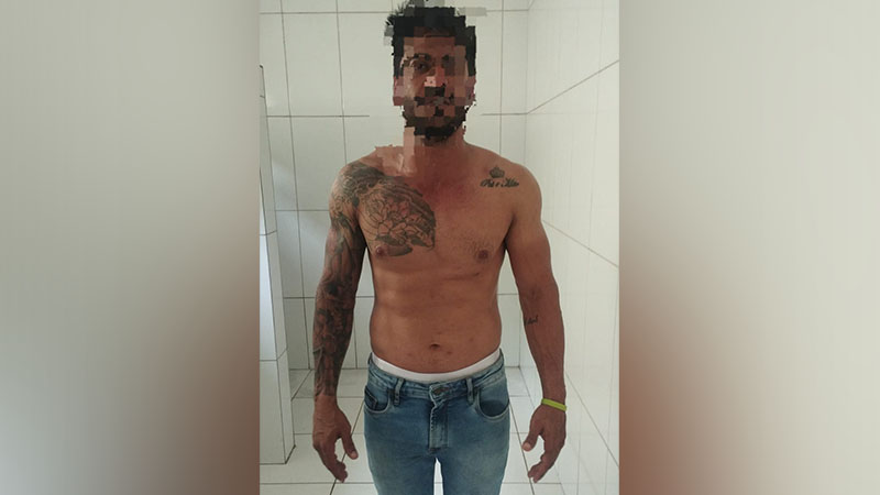 Homem sem camisa, de jeans, com tatuagens e rosto pixelado.