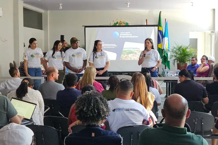 Grupo de pessoas em palco e palestrante com microfone em evento sobre empreendedorismo.