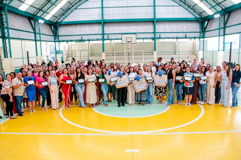 Grande grupo de mulheres e alguns homens em uma quadra poliesportiva, segurando certificados e cestas de prêmios.