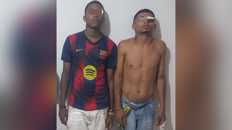 Dois homens com rostos borrados, um vestindo camisa do Barcelona e outro sem camisa, ambos algemados, em frente a uma parede clara.