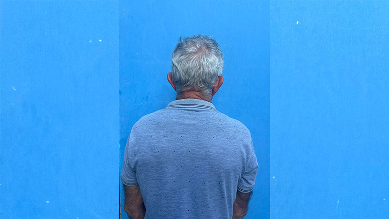 Homem de costas com cabelos grisalhos e camisa cinza contra parede azul.