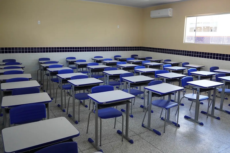 Sala de aula vazia com carteiras azuis e brancas.