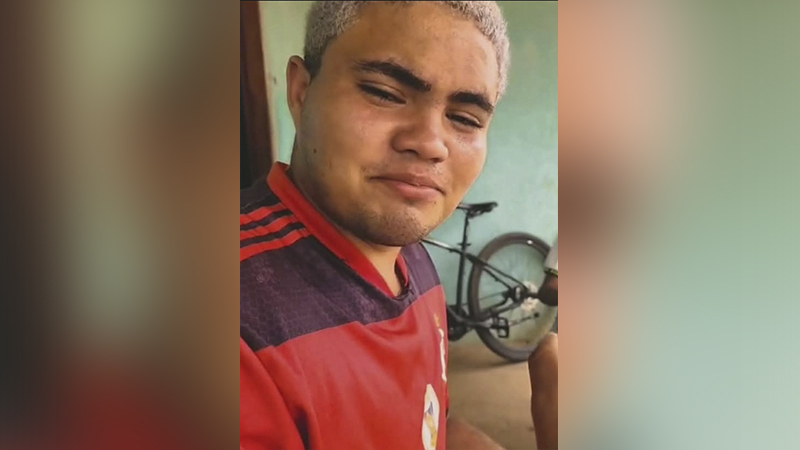 Jovem com cabelo loiro platinado e camisa rubro-negra, sorrindo sutilmente.